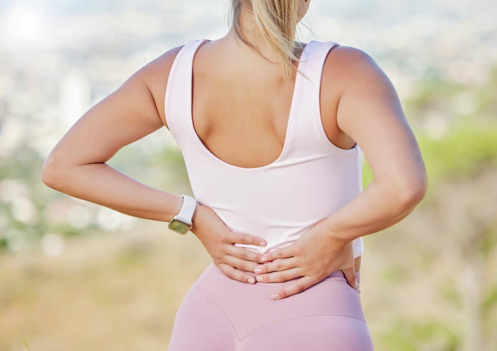 Back pain, hands and woman exercise outdoor, wellness or muscle tension. Healthy female, athlete an.
